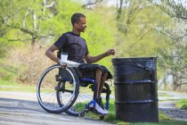 Человек в инвалидном кресле, у которого был менингит, выбрасывающий мусор в парке — стоковое фото