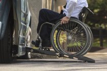 Homme d'affaires atteint de dystrophie musculaire en fauteuil roulant entrant dans son van accessible dans le parking — Photo de stock