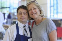 Hombre con Síndrome de Down trabajando en una tienda de comestibles y abrazándose con la mujer - foto de stock