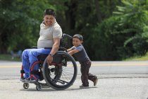 Латиноамериканець зі спінальним Кордом Убивцею у кріслі на колесах зі своїм сином. — стокове фото