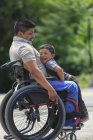 Щасливий іспаномовний чоловік з Спінальним Кордом Убивцею у кріслі на колесах зі своїм сином — стокове фото