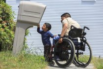 Homme hispanique avec blessure médullaire en fauteuil roulant avec son fils regardant dans une boîte aux lettres — Photo de stock