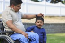 Homme hispanique avec lésion médullaire en fauteuil roulant avec son fils dans la pelouse — Photo de stock