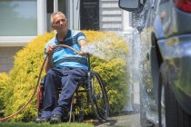Man with a Spinal Cord Injury in wheelchair washing his accessible car — Stock Photo