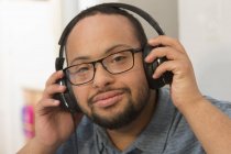 Happy African American man with Down Syndrome listening to music with headphones at home — Stock Photo