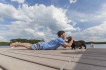 Jeune homme trisomique jouant avec un chien sur un quai — Photo de stock