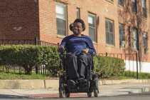 Homem afro-americano feliz com paralisia cerebral usando sua cadeira de rodas poder fora — Fotografia de Stock