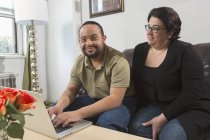 Happy African American man with Down Syndrome using laptop  with mother at home — Stock Photo