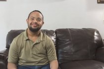 Happy African American man with Down Syndrome sitting on sofa at home — Stock Photo