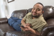 Щасливий афроамериканець людина з синдромом Дауна за допомогою смартфона в домашніх умовах — стокове фото