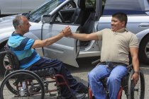 Amis avec blessures de la moelle épinière en fauteuil roulant se saluant — Photo de stock