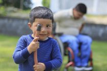 Portrait d'un enfant hispanique tenant un tuyau et de son père en fauteuil roulant avec blessure à la moelle épinière en arrière-plan — Photo de stock