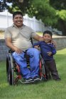 Portrait of Hispanic man with Spinal Cord Injury in wheelchair with his son in lawn — Stock Photo