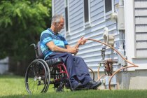 Чоловік з травмою спинного мозку в інвалідному кріслі влаштовує шланг на своєму будинку на задньому дворі — стокове фото