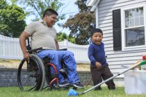 Homem hispânico com lesão medular em cadeira de rodas com seu filho se preparando para lavar um carro — Fotografia de Stock