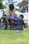 Homme hispanique avec blessure à la moelle épinière en fauteuil roulant avec son fils se préparant à laver une voiture — Photo de stock