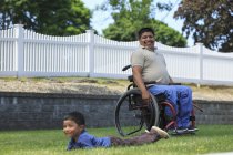 Homme hispanique avec lésion médullaire en fauteuil roulant jouant avec son fils dans la pelouse — Photo de stock