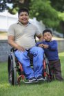 Portrait de l'homme hispanique avec blessure à la moelle épinière en fauteuil roulant avec son fils dans la pelouse — Photo de stock