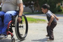 Homem hispânico com lesão medular em cadeira de rodas brincando com seu filho — Fotografia de Stock