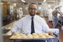 Afro-americano com Síndrome de Down como chef segurando uma bandeja de biscoitos na cozinha comercial — Fotografia de Stock