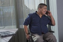 Uomo ispanico con lesione del midollo spinale che parla al telefono in un ufficio — Foto stock