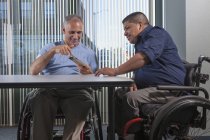 Two men with Spinal Cord Injuries looking at a phone in an office — Stock Photo