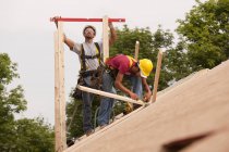 Carpinteros hispanos nivelando tableros en el techo de una casa en construcción - foto de stock