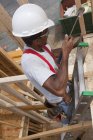 Carpinteiro hispânico usando um martelo em uma escada em uma casa em construção — Fotografia de Stock