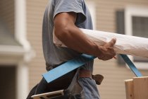 Mid section view of a carpenter carrying a steel square and a blueprint — Stock Photo