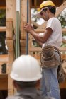 Carpinteros hispanos midiendo un marco con un nivel en una casa en construcción - foto de stock