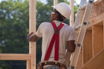 Hispanic carpenter on a ladder checking the framing of a house under construction — Stock Photo
