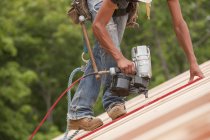 Falegname ispanico con una sparachiodi sui pannelli del tetto — Foto stock
