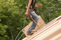 Carpinteiro hispânico transportando bobinas de pregos no telhado de uma casa em construção — Fotografia de Stock