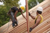 Charpentiers hispaniques plaçant le panneau de toit à une maison en construction — Photo de stock