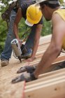 Carpinteiros hispânicos colocando painel de telhado com uma pistola de prego em uma casa em construção — Fotografia de Stock
