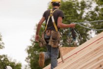 Carpintero hispano caminando en el techo de una casa en construcción - foto de stock