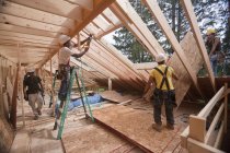 Carpinteiros hispânicos instalando o painel do telhado através do piso superior em uma casa em construção — Fotografia de Stock