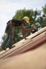 Carpinteiro hispânico usando uma pistola de prego na cobertura de uma casa em construção — Fotografia de Stock