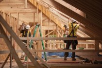 Hispanic carpenters bringing sheathing to roof at a house under construction — Stock Photo