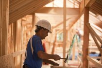 Carpintero hispano clavando clavos a bordo en una casa en construcción - foto de stock