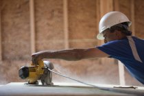 Carpinteiro hispânico usando uma serra circular no revestimento do telhado em uma casa em construção — Fotografia de Stock