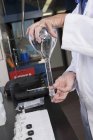 Imagen recortada del científico que mezcla el contenido líquido del matraz invirtiendo el matraz en el laboratorio de la planta de tratamiento de agua - foto de stock