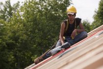 Hispanic carpenter resting on the roof construction of a house with a nail gun — Stock Photo