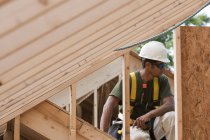 Charpentier hispanique tenant un mètre ruban à l'étage supérieur dans une maison en construction — Photo de stock
