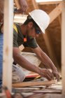 Charpentier hispanique marquant une mesure sur une planche dans une maison en construction — Photo de stock