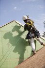 Hispanic carpenter using a nail gun on the roof trim of a house under construction — Stock Photo