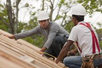 Carpinteros hispanos trabajando con una pistola de clavos en el techo de una casa en construcción - foto de stock