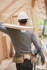 Carpenter carrying a board at a building construction site — Stock Photo