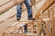 Hispanic carpenters pulling up air hose while standing on support board at a house under construction — Stock Photo