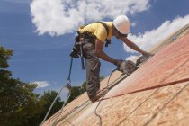 Hispanic carpenter using a circular saw on a roof sheathing at a house under construction — Stock Photo